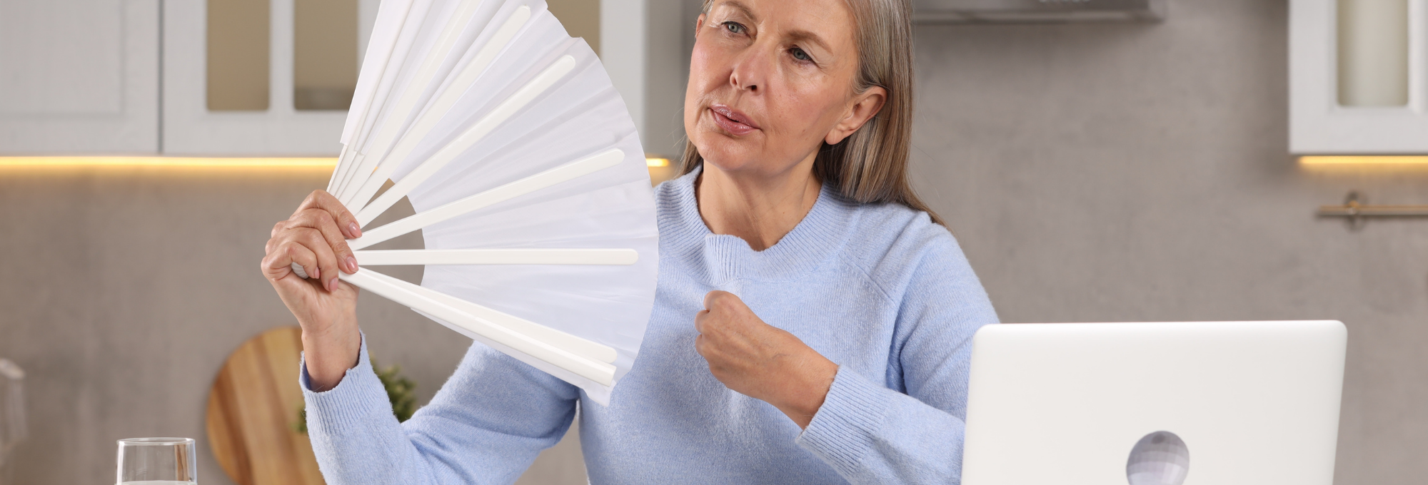 Ältere Frau hat einen Fächer in der Hand und wedelt sich Luft zu, um ihre Hitzewallungen zu bekämpfen.